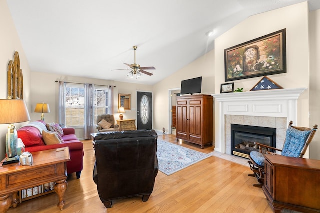 living room featuring ceiling fan, lofted ceiling, a tiled fireplace, and light wood-type flooring