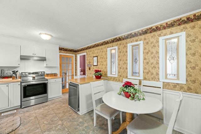 kitchen with stainless steel appliances, wood counters, a textured ceiling, white cabinets, and ornamental molding