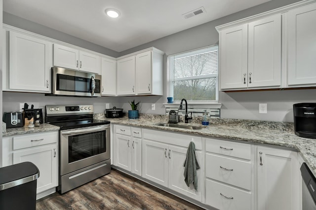 kitchen with sink, white cabinetry, dark hardwood / wood-style flooring, stainless steel appliances, and light stone countertops