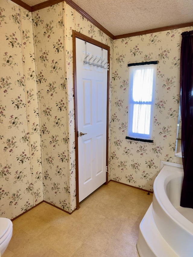 bathroom with ornamental molding, toilet, a textured ceiling, and a tub to relax in