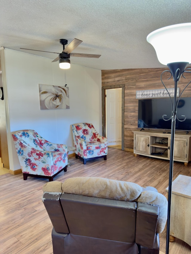 living room featuring ceiling fan, hardwood / wood-style flooring, a textured ceiling, and wood walls