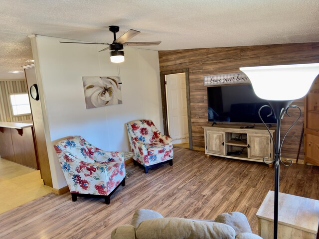 living room featuring hardwood / wood-style flooring, ceiling fan, a textured ceiling, and wood walls