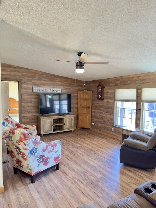 living room with ceiling fan, light hardwood / wood-style floors, a textured ceiling, vaulted ceiling, and wood walls