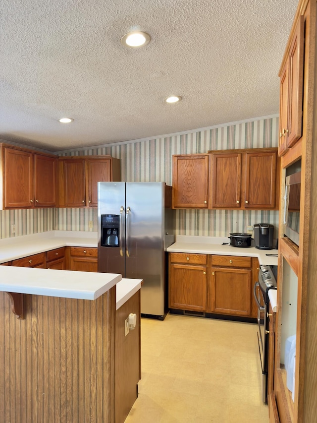 kitchen with stainless steel appliances, a breakfast bar, a textured ceiling, and kitchen peninsula