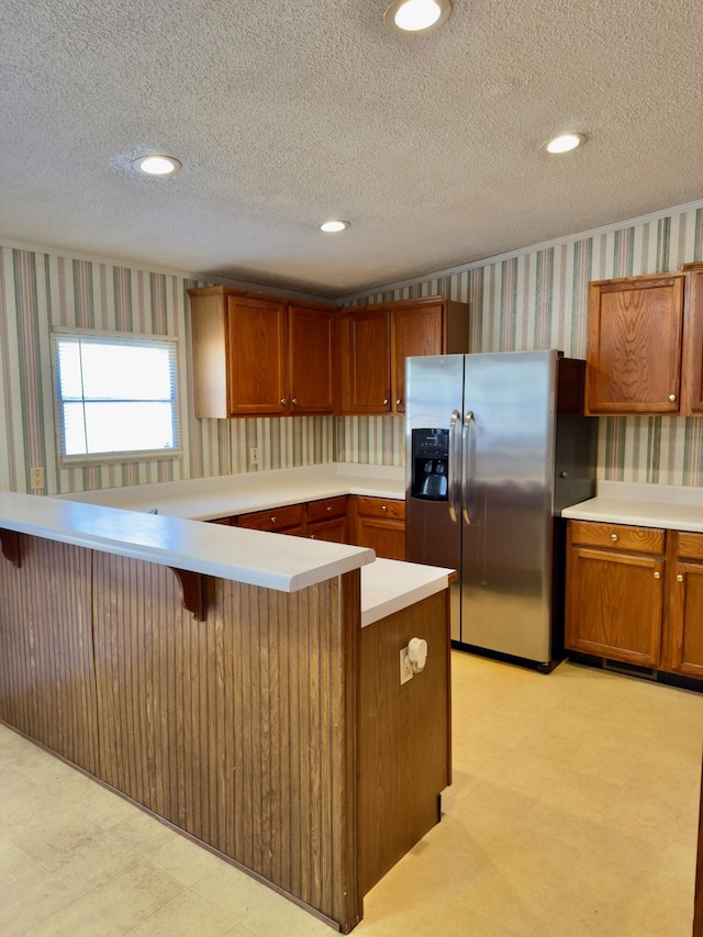 kitchen featuring a breakfast bar, stainless steel fridge, kitchen peninsula, and a textured ceiling