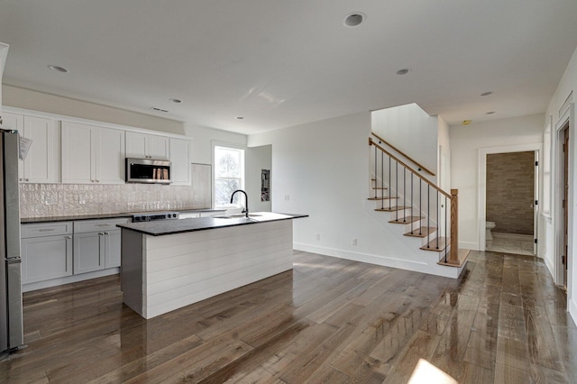 kitchen featuring white cabinetry, an island with sink, appliances with stainless steel finishes, decorative backsplash, and sink