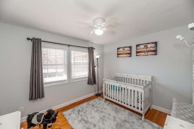 bedroom featuring light hardwood / wood-style flooring, a crib, and ceiling fan