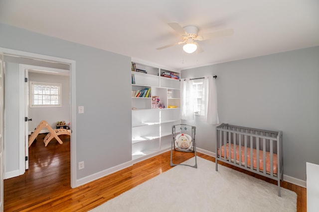 bedroom featuring wood-type flooring, a crib, and ceiling fan