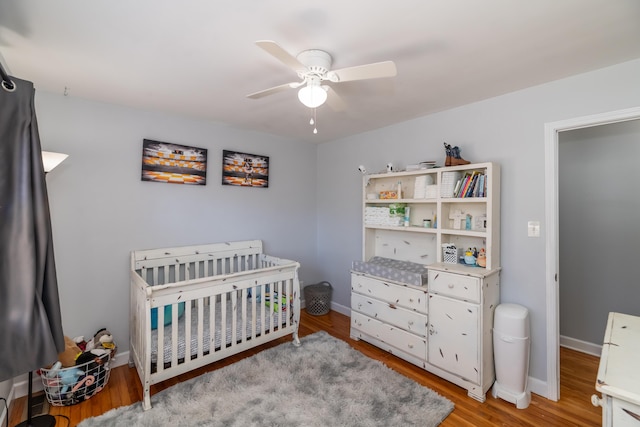 bedroom featuring a nursery area, light wood-type flooring, and ceiling fan