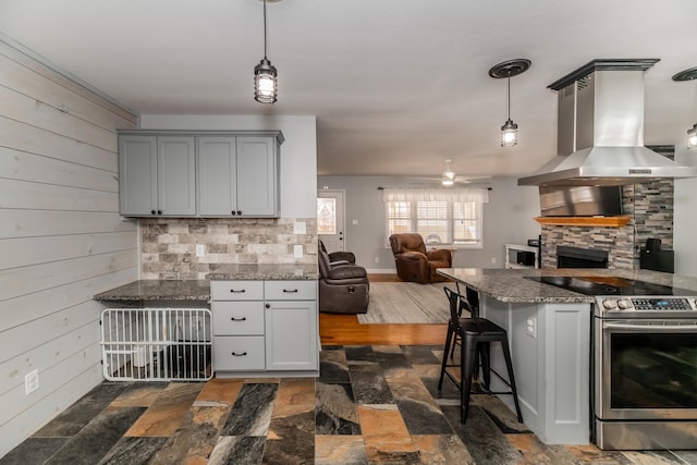 kitchen featuring wood walls, island exhaust hood, stainless steel range with electric cooktop, and decorative light fixtures