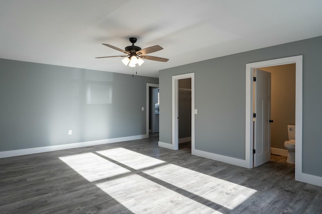 unfurnished bedroom featuring a walk in closet, ensuite bathroom, and dark wood-type flooring