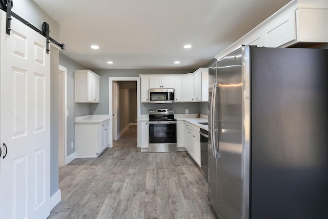 kitchen with a barn door, light hardwood / wood-style floors, white cabinetry, and appliances with stainless steel finishes