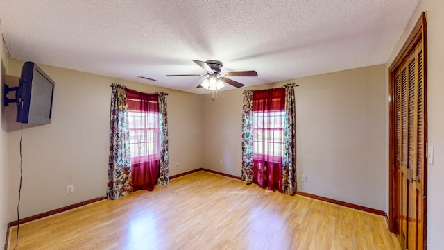 unfurnished bedroom with ceiling fan, light hardwood / wood-style floors, a textured ceiling, and multiple windows