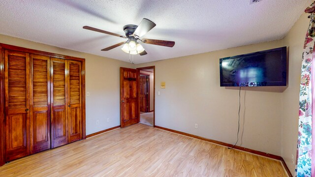 unfurnished bedroom with ceiling fan, a closet, light hardwood / wood-style floors, and a textured ceiling