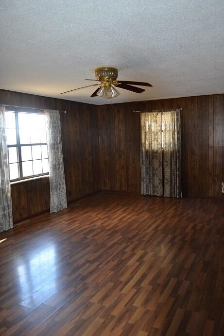 empty room featuring ceiling fan, wooden walls, dark wood-type flooring, and a textured ceiling