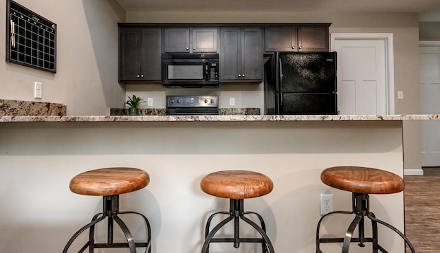 kitchen with dark brown cabinets, dark hardwood / wood-style floors, a breakfast bar area, and black appliances