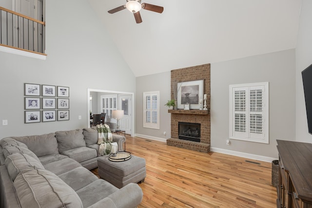 living room featuring high vaulted ceiling, light hardwood / wood-style flooring, a brick fireplace, and ceiling fan