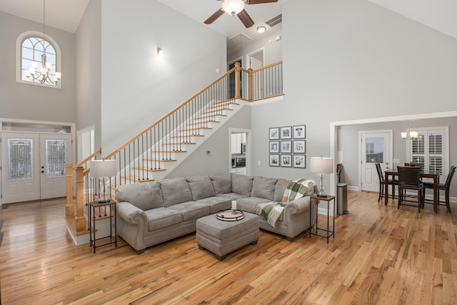 living room featuring high vaulted ceiling, french doors, light wood-type flooring, and ceiling fan with notable chandelier