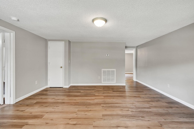 spare room with a textured ceiling, light wood-style flooring, visible vents, and baseboards