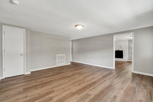 unfurnished room featuring a textured ceiling, visible vents, baseboards, light wood-style floors, and a brick fireplace