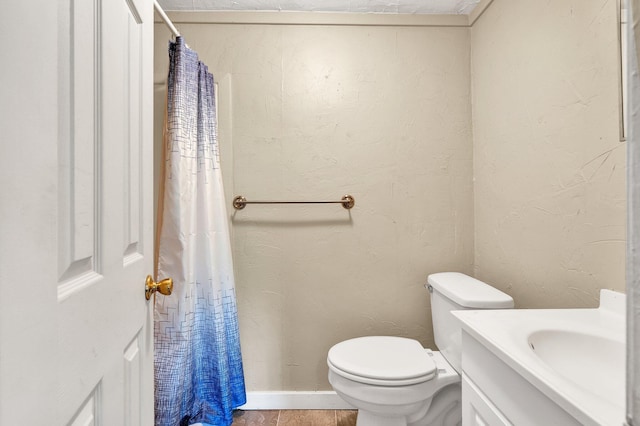 full bath featuring toilet, a textured wall, and vanity