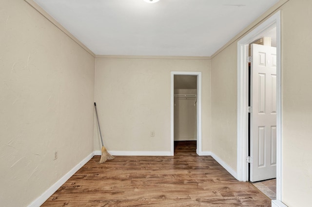 unfurnished room with a textured wall, ornamental molding, wood finished floors, and baseboards