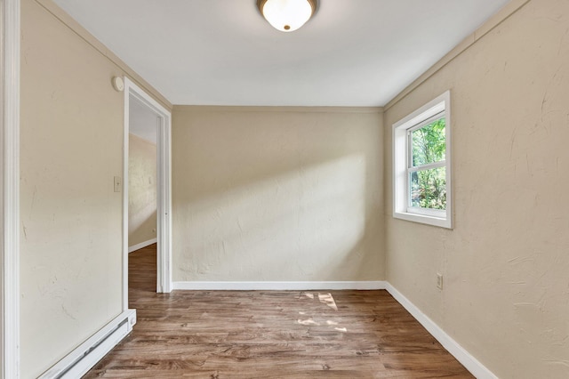 unfurnished room with a baseboard radiator, baseboards, wood finished floors, and a textured wall