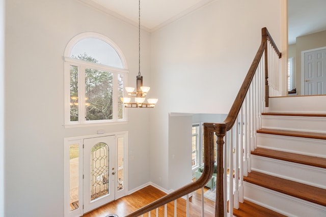 foyer entrance with crown molding, a healthy amount of sunlight, a notable chandelier, and hardwood / wood-style flooring