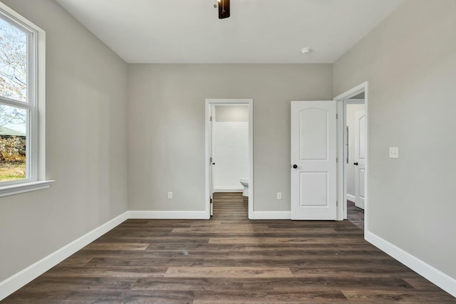 unfurnished bedroom with connected bathroom, multiple windows, ceiling fan, and dark hardwood / wood-style floors