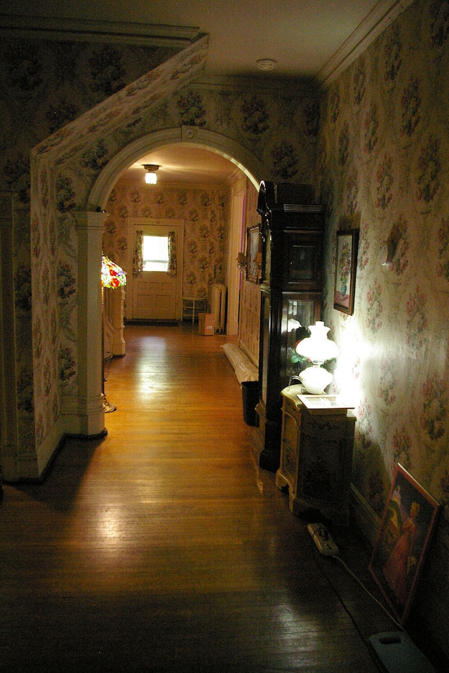 corridor featuring arched walkways, crown molding, wood finished floors, and wallpapered walls