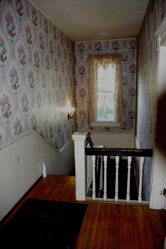 stairway with wood finished floors and wallpapered walls