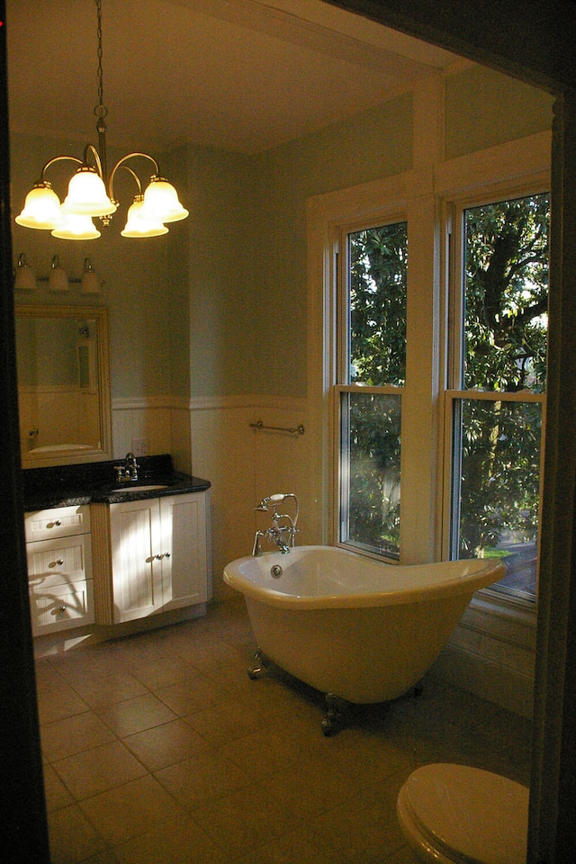 bathroom featuring a notable chandelier, a wainscoted wall, vanity, a soaking tub, and tile patterned floors