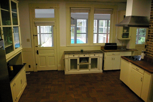 kitchen with black electric cooktop, white cabinets, range hood, dark countertops, and plenty of natural light