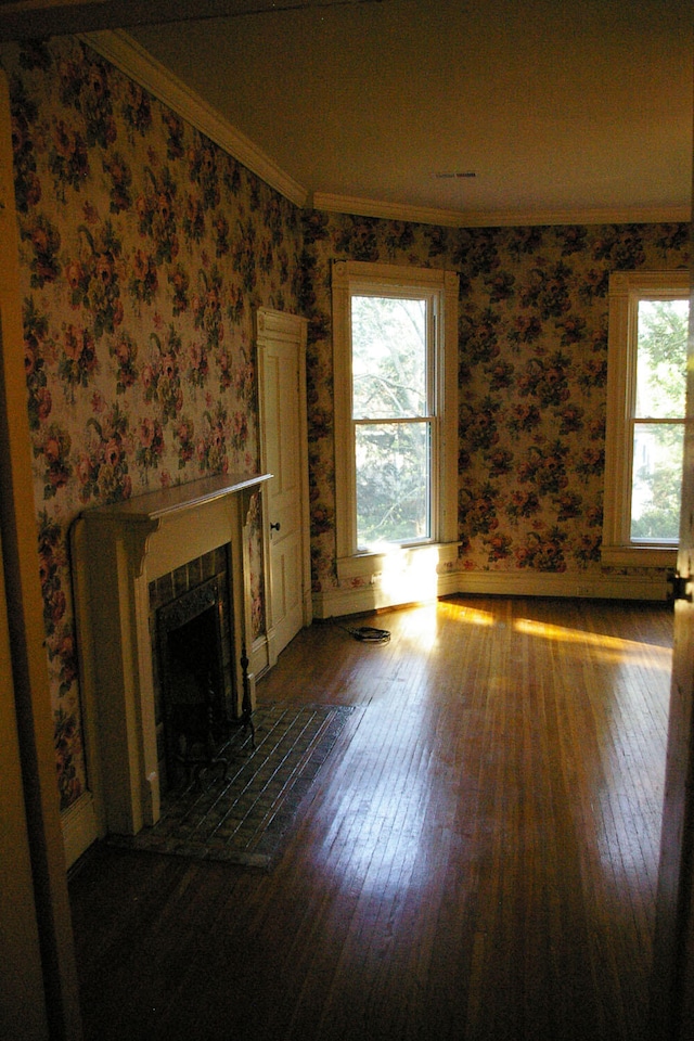 unfurnished living room featuring crown molding, a tiled fireplace, wood-type flooring, and wallpapered walls