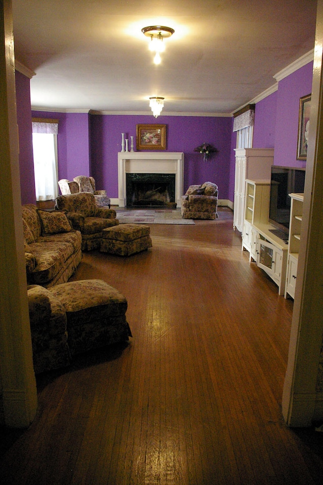 living room with dark wood-style floors, a fireplace with raised hearth, and crown molding