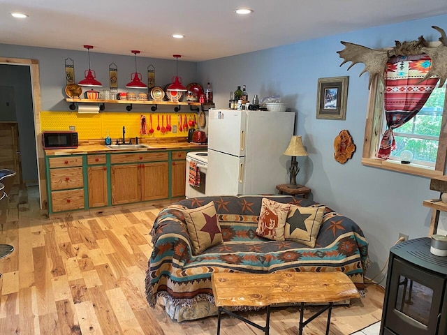 kitchen with decorative light fixtures, light wood-type flooring, white appliances, and sink