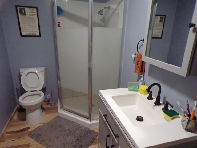 bathroom with a shower with door, vanity, wood-type flooring, and toilet