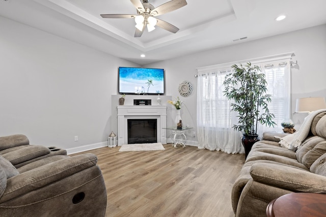 living room with a raised ceiling, ceiling fan, and light hardwood / wood-style flooring