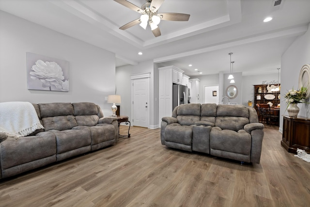 living room with ceiling fan, light wood-type flooring, and a tray ceiling