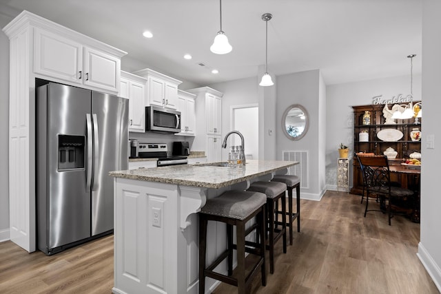 kitchen featuring appliances with stainless steel finishes, decorative light fixtures, sink, light stone countertops, and a center island with sink