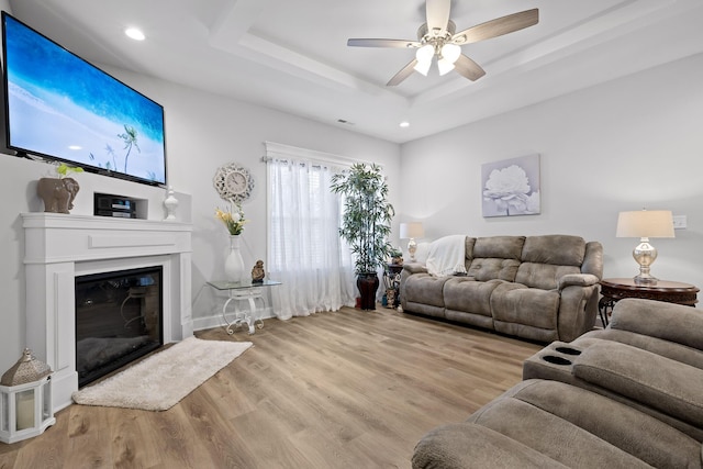 living room with a tray ceiling, light hardwood / wood-style floors, and ceiling fan