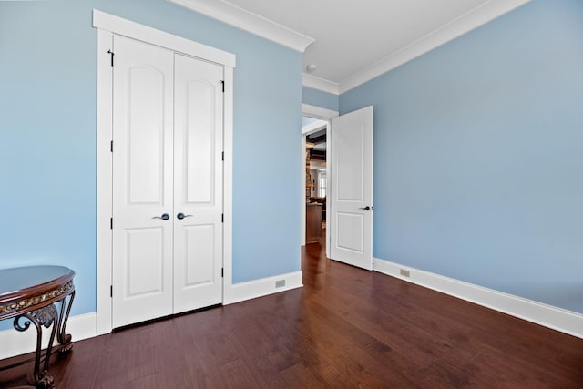 unfurnished bedroom with dark wood-type flooring, crown molding, and a closet