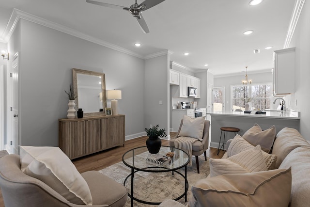 living area with ceiling fan with notable chandelier, ornamental molding, recessed lighting, baseboards, and light wood-style floors