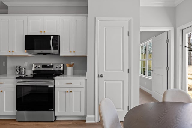 kitchen with white cabinetry, ornamental molding, and stainless steel appliances