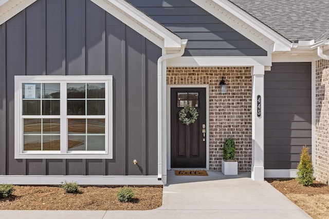 doorway to property with roof with shingles, brick siding, and board and batten siding
