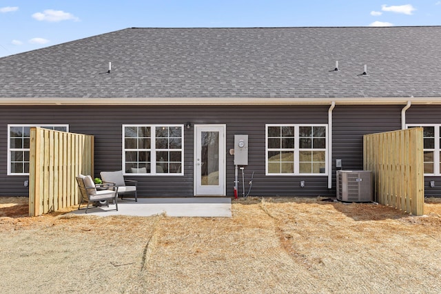 rear view of house with central AC unit, a patio area, and a shingled roof