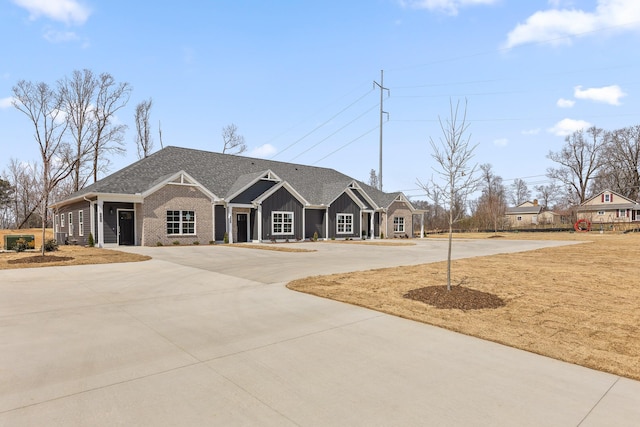 view of front of home featuring curved driveway, a shingled roof, brick siding, and board and batten siding