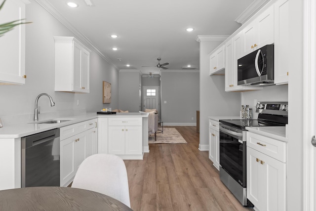 kitchen with a peninsula, a sink, ceiling fan, appliances with stainless steel finishes, and ornamental molding