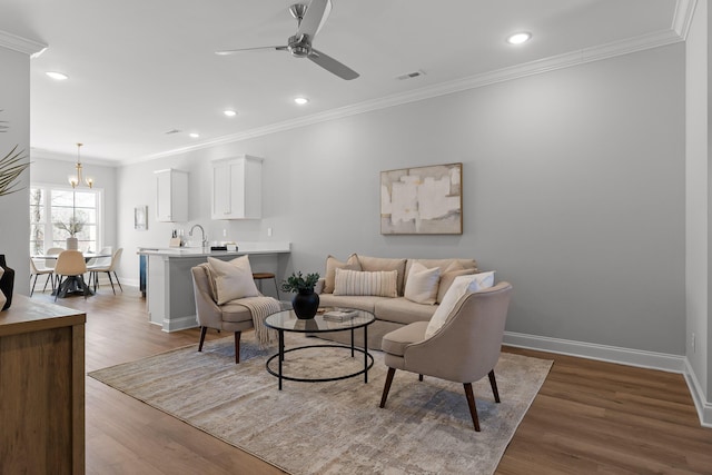 living area featuring ornamental molding, ceiling fan with notable chandelier, baseboards, and wood finished floors