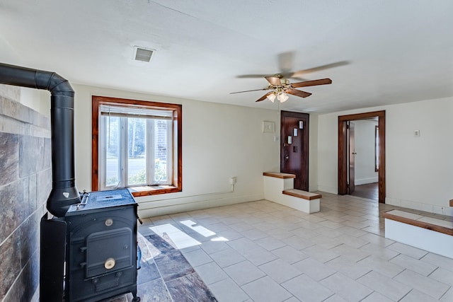 unfurnished living room featuring ceiling fan, light tile patterned flooring, and a wood stove